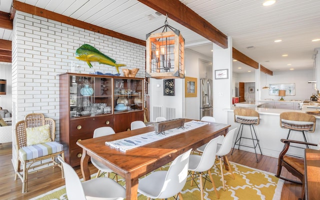 dining space with beamed ceiling, brick wall, and light hardwood / wood-style floors