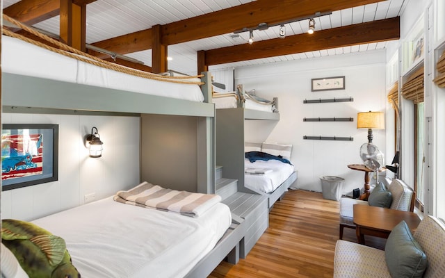 bedroom featuring track lighting, beamed ceiling, and light wood-type flooring