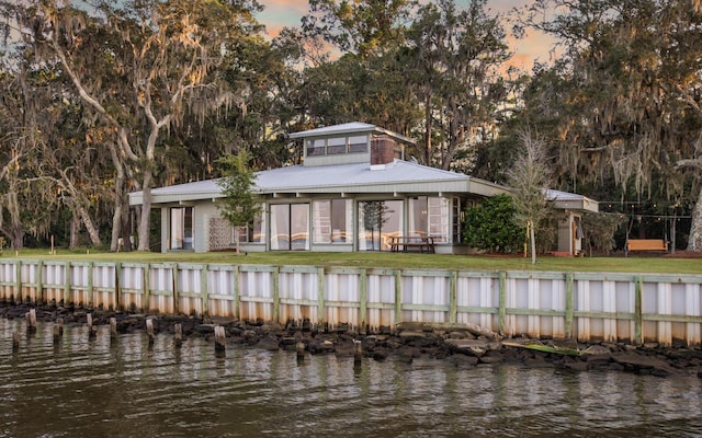 back house at dusk featuring a water view and a yard