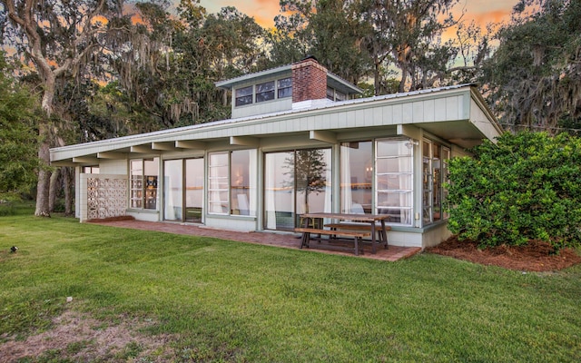 back house at dusk featuring a patio and a lawn