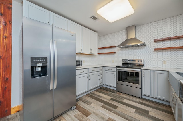 kitchen with appliances with stainless steel finishes, wall chimney exhaust hood, light hardwood / wood-style flooring, and backsplash