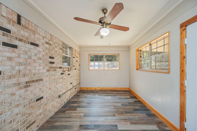 empty room with ornamental molding, brick wall, dark hardwood / wood-style floors, and ceiling fan