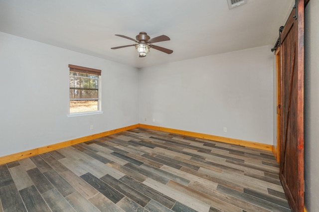 unfurnished room featuring dark wood-type flooring, a barn door, and ceiling fan