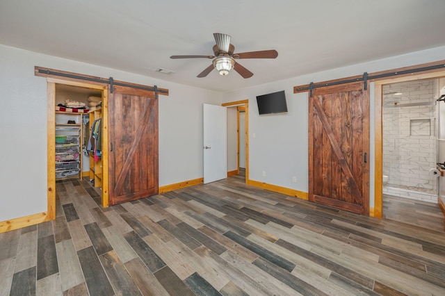 unfurnished bedroom with a closet, a barn door, dark wood-type flooring, and a spacious closet