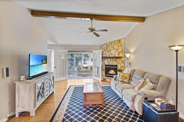 living room featuring light hardwood / wood-style flooring, ceiling fan, a fireplace, lofted ceiling with beams, and a textured ceiling