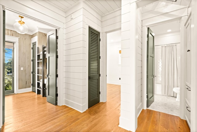 corridor with ornamental molding, light hardwood / wood-style floors, and wood walls