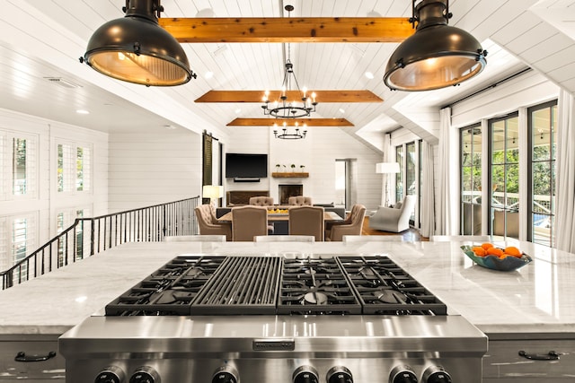 kitchen featuring wood walls, an inviting chandelier, decorative light fixtures, beamed ceiling, and light stone countertops