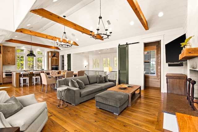 living room featuring lofted ceiling with beams, an inviting chandelier, a barn door, and hardwood / wood-style floors