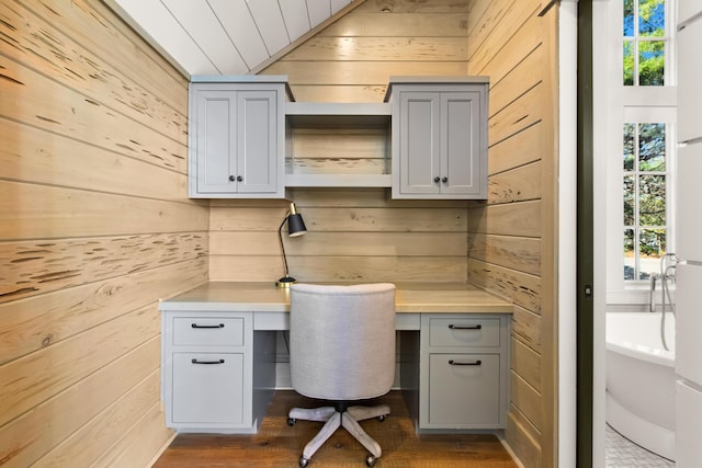 unfurnished office featuring lofted ceiling, plenty of natural light, wooden walls, and built in desk