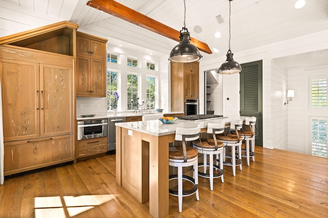 kitchen featuring hanging light fixtures, a kitchen island, stainless steel appliances, light hardwood / wood-style floors, and a kitchen bar