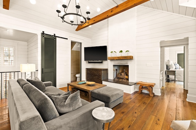 living room featuring a fireplace, a notable chandelier, a barn door, dark wood-type flooring, and beam ceiling