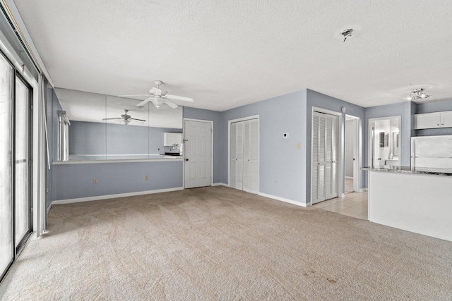 unfurnished living room with ceiling fan, light colored carpet, and a textured ceiling