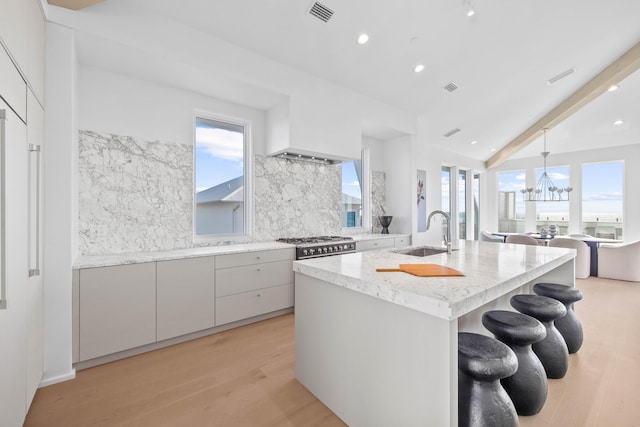 kitchen with a center island with sink, tasteful backsplash, a sink, light wood-type flooring, and plenty of natural light