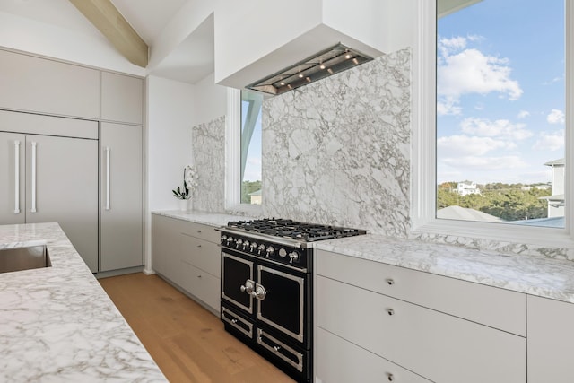 kitchen with light stone counters, light wood finished floors, backsplash, wall chimney range hood, and high quality appliances