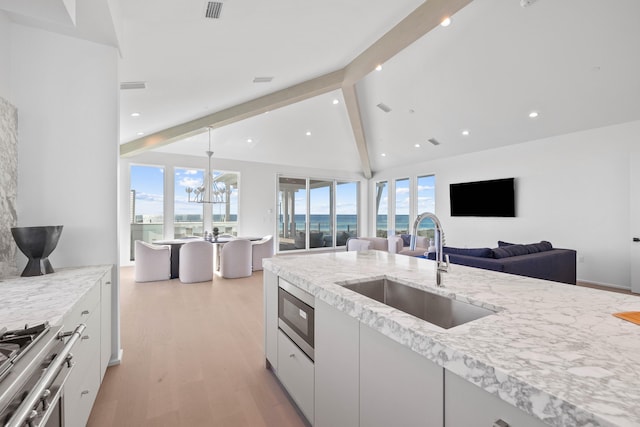 kitchen with stainless steel microwave, lofted ceiling with beams, light wood-style flooring, a sink, and range