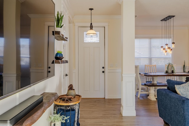 foyer entrance featuring ornamental molding, decorative columns, and light wood-type flooring