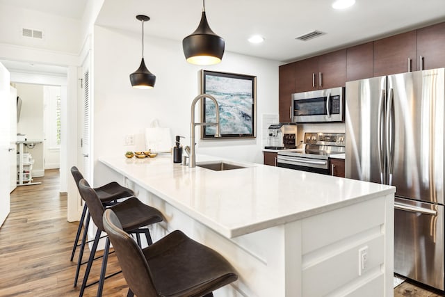 kitchen featuring pendant lighting, sink, appliances with stainless steel finishes, dark brown cabinets, and a kitchen breakfast bar