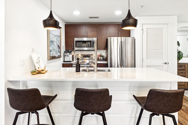 kitchen featuring a breakfast bar, dark brown cabinets, hanging light fixtures, stainless steel appliances, and light hardwood / wood-style floors