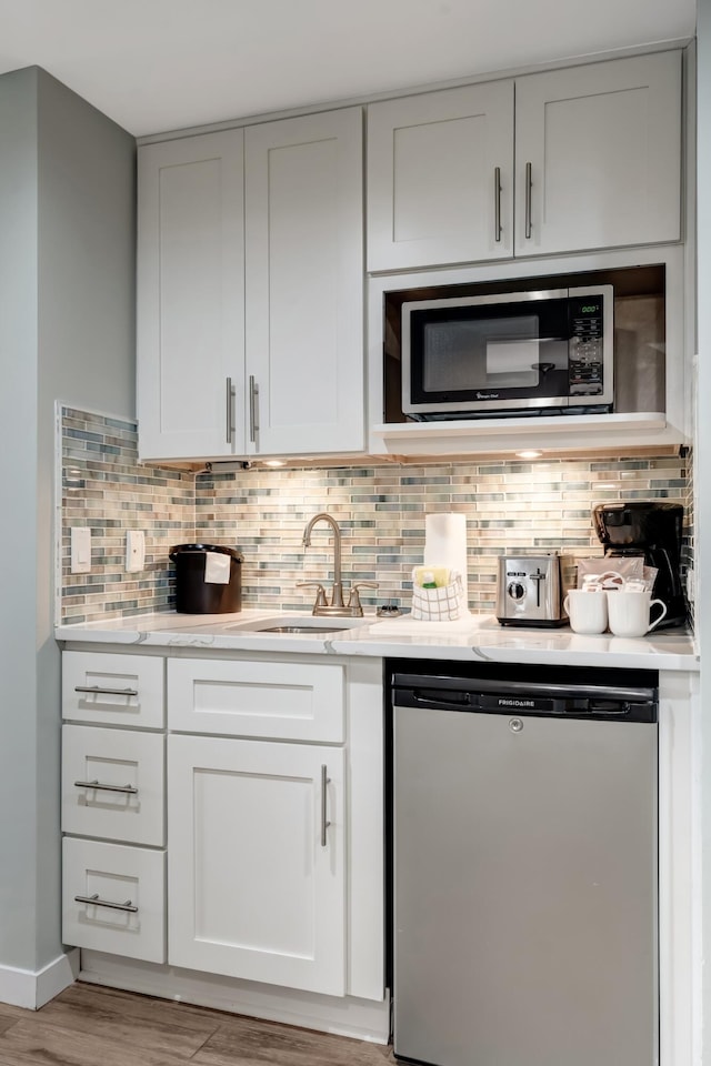 kitchen with white cabinetry, dishwashing machine, sink, and backsplash