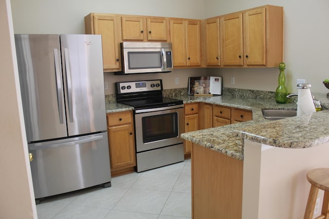 kitchen with light tile patterned flooring, sink, appliances with stainless steel finishes, a kitchen breakfast bar, and kitchen peninsula