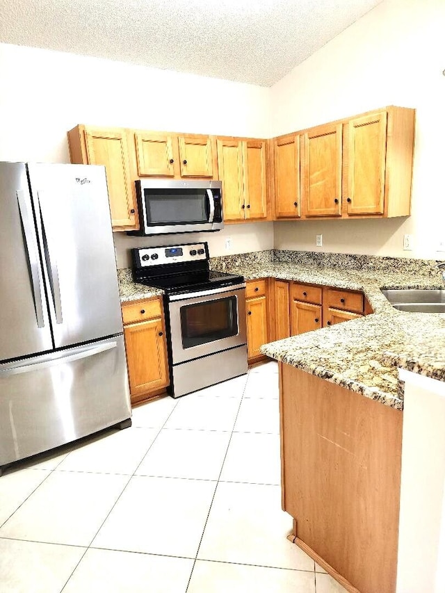 kitchen featuring appliances with stainless steel finishes, sink, light tile patterned floors, light stone counters, and a textured ceiling