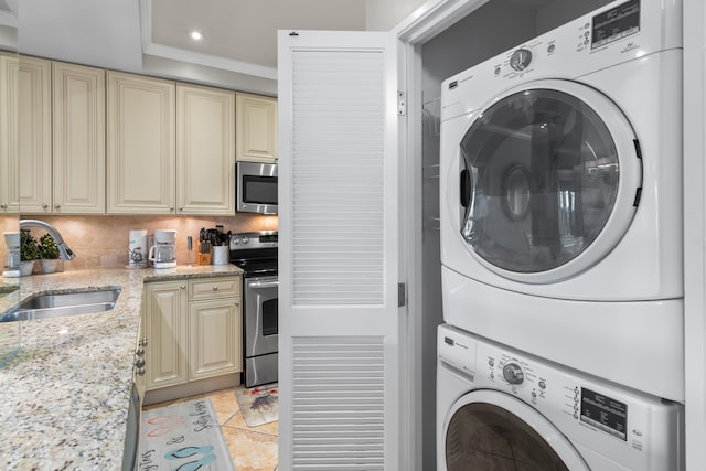 clothes washing area featuring crown molding, stacked washer and clothes dryer, sink, and light tile patterned floors