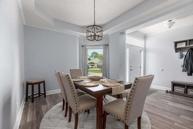 dining area with wood-type flooring, a notable chandelier, a tray ceiling, crown molding, and a textured ceiling