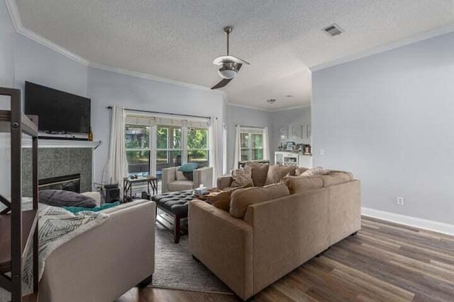 living room featuring dark wood-type flooring, crown molding, a tiled fireplace, and a textured ceiling