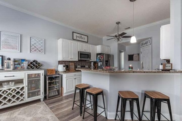 kitchen with appliances with stainless steel finishes, white cabinets, beverage cooler, kitchen peninsula, and light hardwood / wood-style flooring