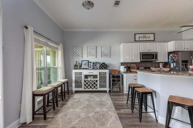 kitchen featuring hardwood / wood-style floors, stainless steel appliances, wine cooler, ornamental molding, and white cabinets