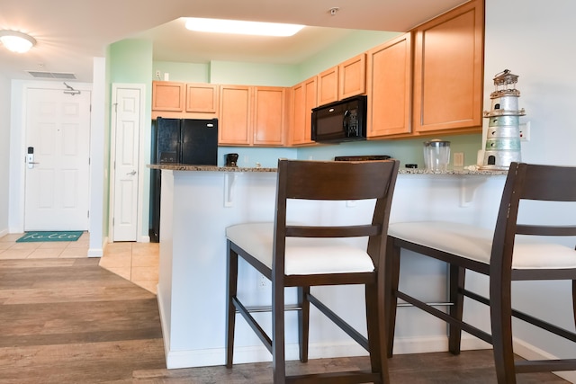 kitchen with a breakfast bar area, light tile patterned floors, kitchen peninsula, light stone countertops, and black appliances