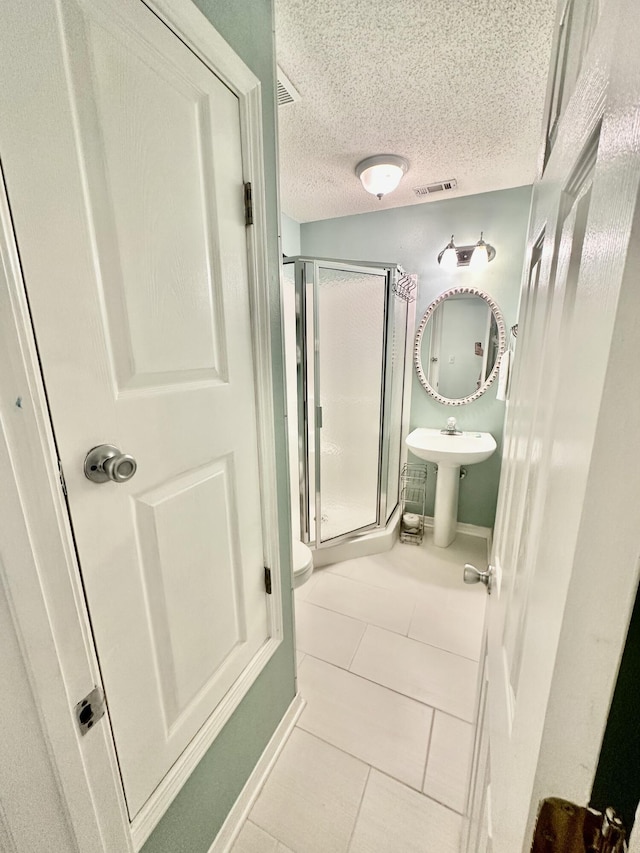 bathroom with walk in shower, tile patterned floors, toilet, sink, and a textured ceiling