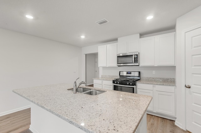 kitchen featuring appliances with stainless steel finishes, sink, white cabinets, a kitchen island with sink, and light stone counters