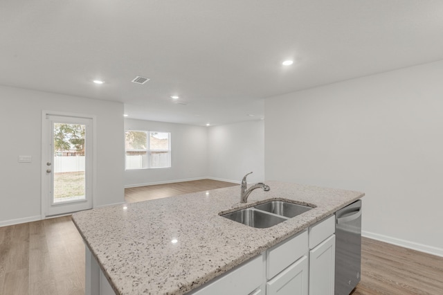 kitchen featuring dishwasher, sink, white cabinets, light stone counters, and a center island with sink