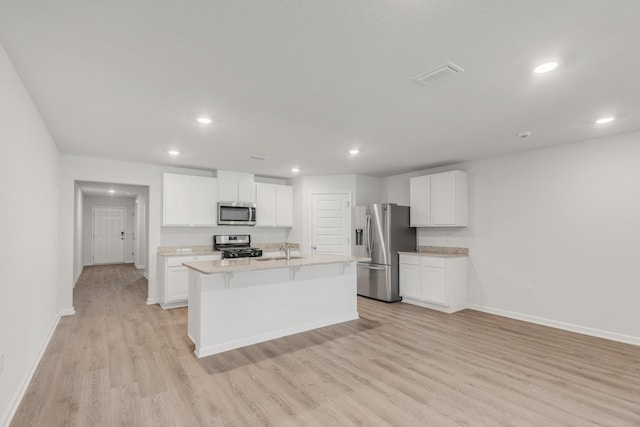 kitchen featuring sink, light stone counters, a center island with sink, stainless steel appliances, and white cabinets
