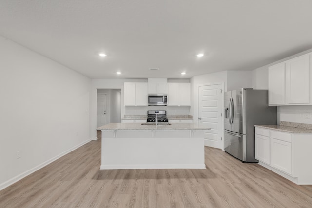 kitchen featuring light stone counters, light hardwood / wood-style flooring, a center island with sink, appliances with stainless steel finishes, and white cabinets