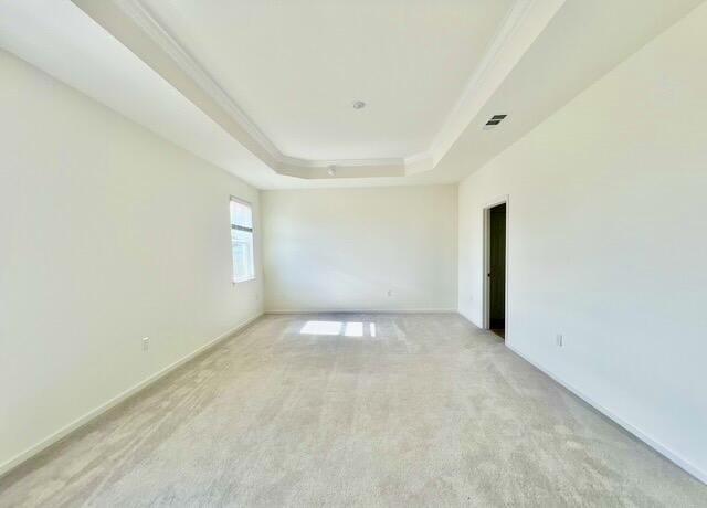 empty room featuring light colored carpet, ornamental molding, and a tray ceiling