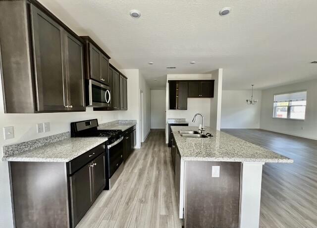 kitchen with sink, light stone counters, light wood-type flooring, appliances with stainless steel finishes, and an island with sink