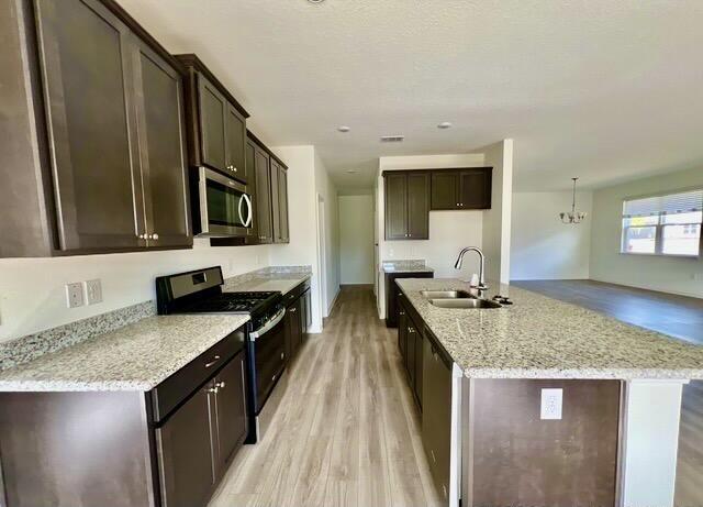 kitchen with sink, stainless steel appliances, light stone counters, dark brown cabinetry, and light wood-type flooring