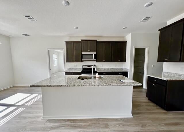 kitchen with stainless steel appliances, light hardwood / wood-style floors, sink, and a center island with sink