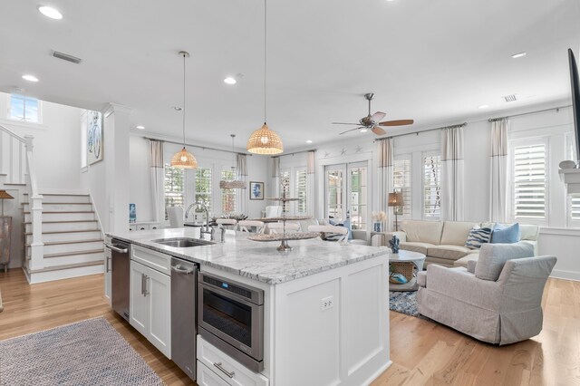 kitchen with sink, white cabinetry, decorative light fixtures, light stone countertops, and a kitchen island with sink