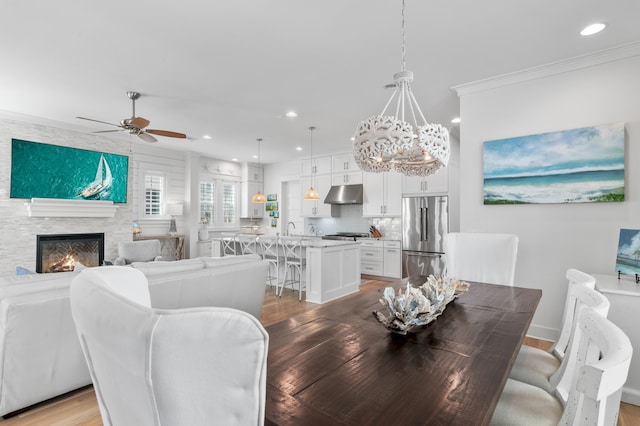 dining space with sink, crown molding, light hardwood / wood-style flooring, a large fireplace, and ceiling fan