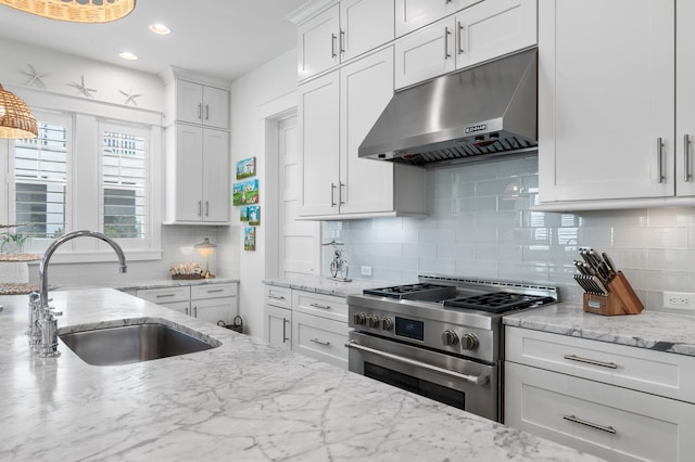 kitchen featuring sink, light stone counters, stainless steel range, white cabinets, and backsplash