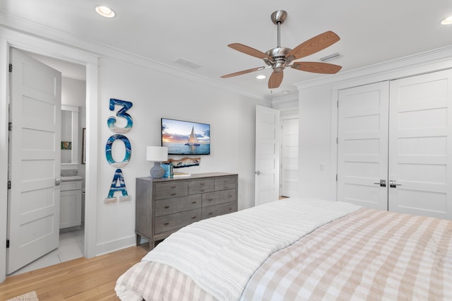 bedroom featuring light wood-type flooring, ornamental molding, ceiling fan, ensuite bath, and a closet