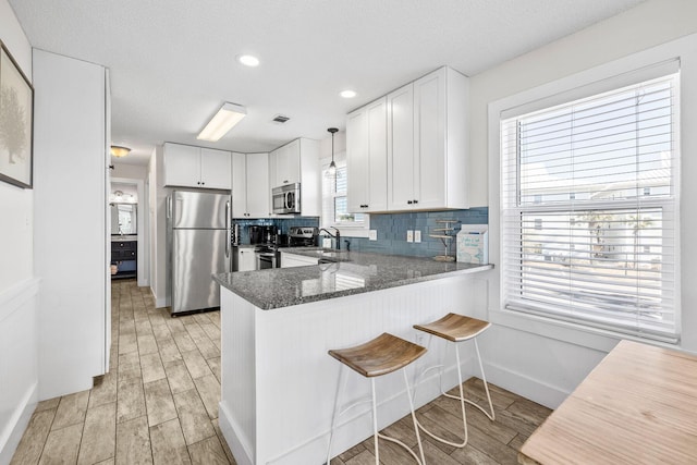 kitchen featuring white cabinetry, stainless steel appliances, kitchen peninsula, and dark stone countertops