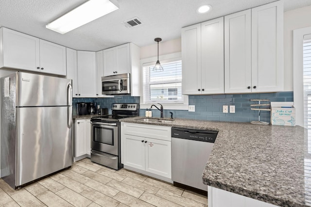 kitchen with sink, white cabinetry, pendant lighting, stainless steel appliances, and backsplash