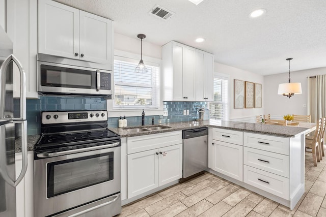 kitchen featuring sink, appliances with stainless steel finishes, kitchen peninsula, pendant lighting, and white cabinets