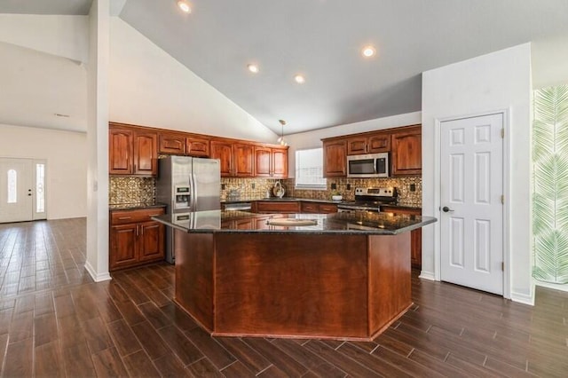 kitchen featuring appliances with stainless steel finishes, pendant lighting, tasteful backsplash, dark stone counters, and a center island