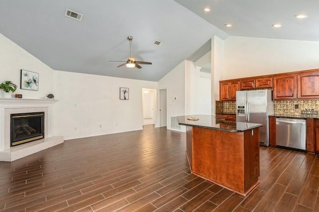 kitchen with dark wood-type flooring, a kitchen island, ceiling fan, stainless steel appliances, and a fireplace