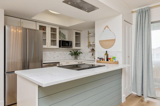 kitchen with light stone counters, stainless steel appliances, kitchen peninsula, and white cabinets